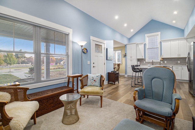 living area with recessed lighting, light wood-type flooring, baseboards, and high vaulted ceiling