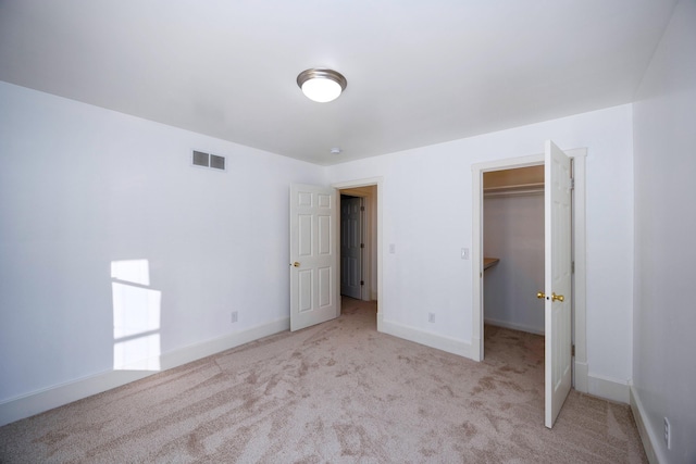 unfurnished bedroom featuring a spacious closet, light colored carpet, and a closet