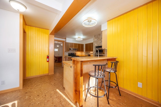 kitchen with butcher block countertops, wood walls, a kitchen bar, kitchen peninsula, and stainless steel appliances