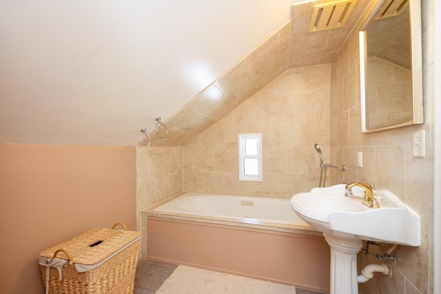 bathroom with tile patterned floors, a bath, vaulted ceiling, and tile walls