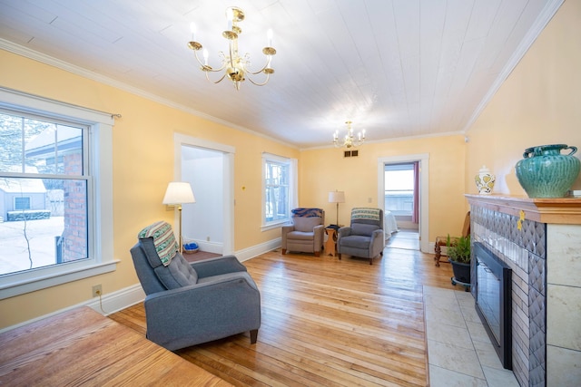 living room with a tiled fireplace, ornamental molding, a chandelier, and light wood-type flooring