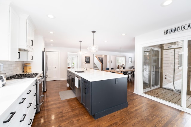 kitchen featuring a kitchen island with sink, stainless steel appliances, white cabinetry, pendant lighting, and a sink