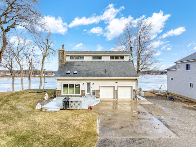 rear view of property with a yard, a chimney, a water view, an attached garage, and driveway