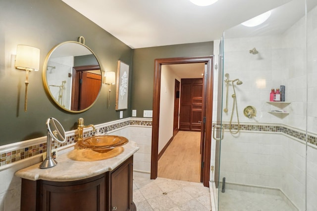 bathroom featuring a stall shower, vanity, a wainscoted wall, and tile walls