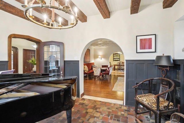 living area featuring a chandelier, arched walkways, beam ceiling, and a wainscoted wall