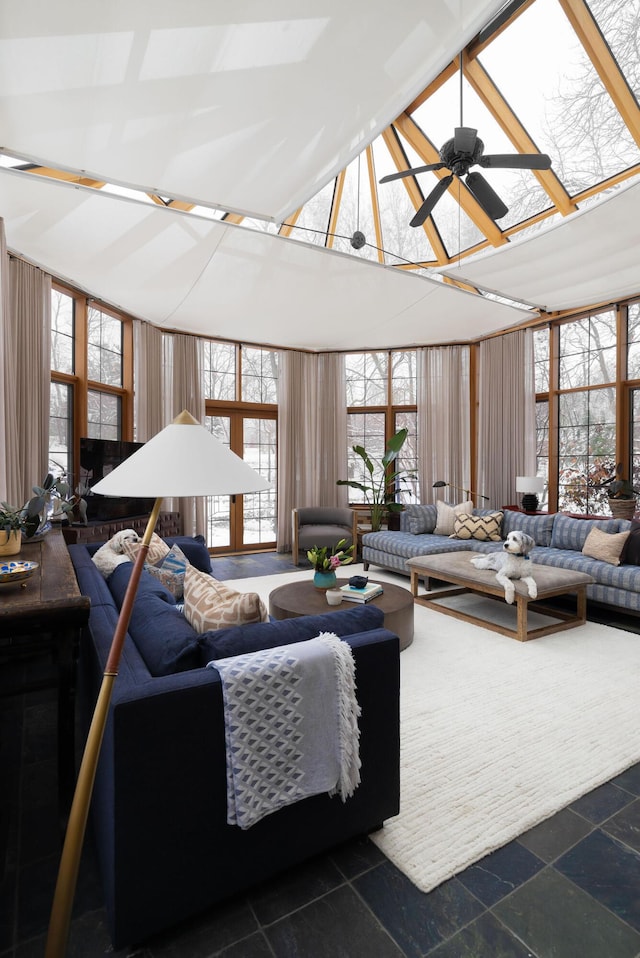 living room with stone tile floors, ceiling fan, and a wall of windows