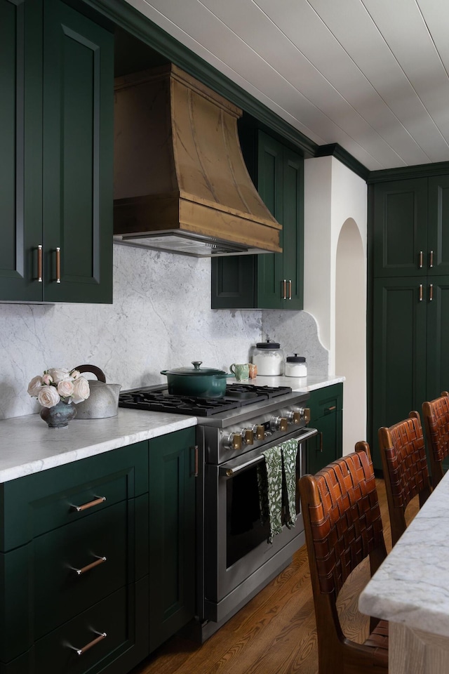 kitchen featuring dark wood finished floors, high end stove, custom exhaust hood, decorative backsplash, and green cabinetry