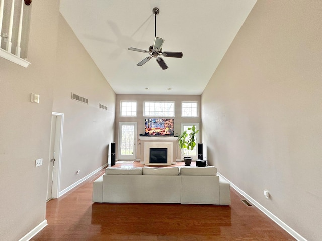 unfurnished living room featuring ceiling fan, wood-type flooring, and a towering ceiling