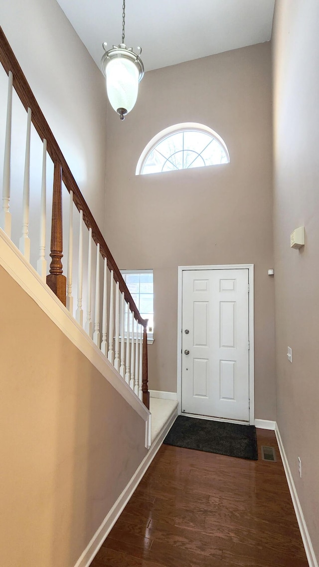 entryway with dark wood-type flooring and a towering ceiling