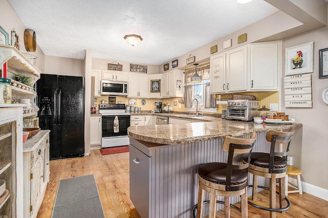 kitchen featuring stainless steel appliances, light wood finished floors, a peninsula, and white cabinetry