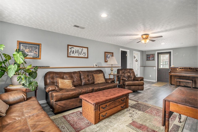 living room featuring visible vents, a ceiling fan, a textured ceiling, wood finished floors, and baseboards