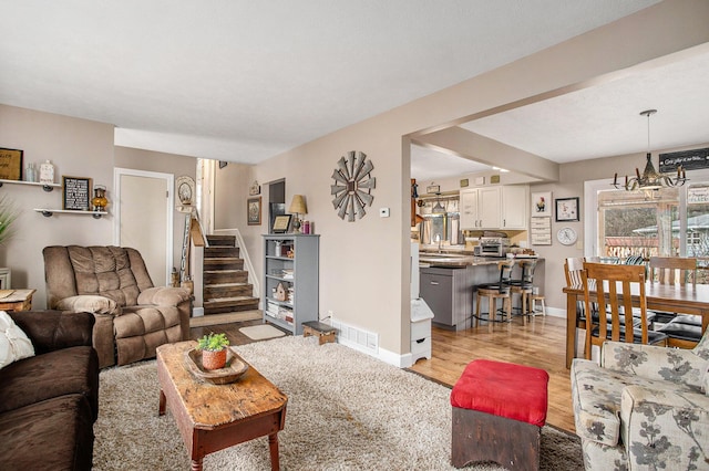 living area featuring visible vents, baseboards, light wood-style flooring, stairs, and a notable chandelier