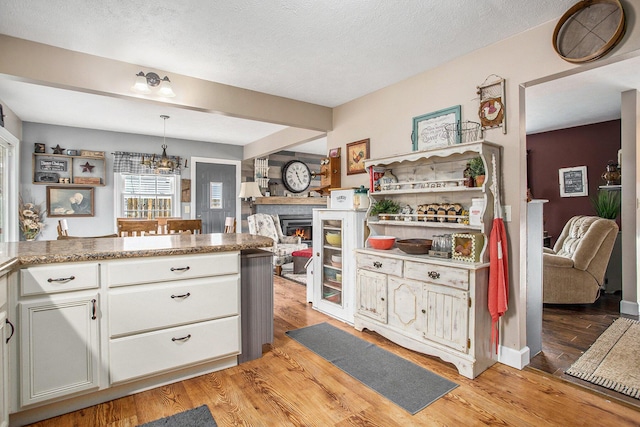 kitchen featuring light wood-type flooring, a warm lit fireplace, and a textured ceiling