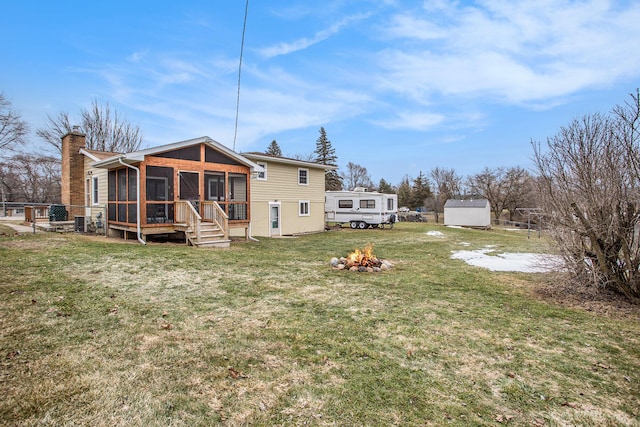 rear view of property with a fire pit, a sunroom, a chimney, a storage unit, and an outdoor structure