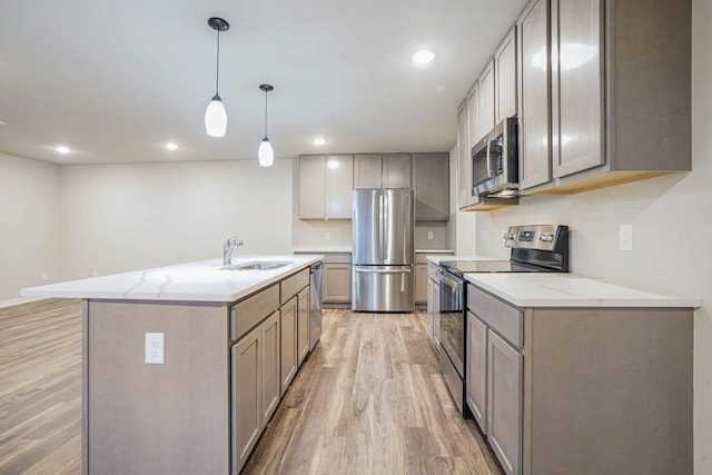 kitchen with appliances with stainless steel finishes, sink, hanging light fixtures, light stone countertops, and a center island with sink