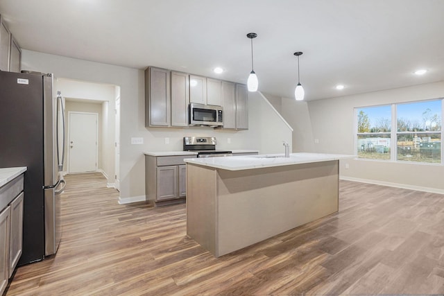 kitchen with pendant lighting, appliances with stainless steel finishes, hardwood / wood-style floors, and a center island with sink