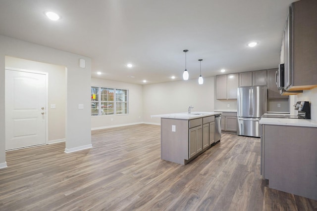 kitchen featuring decorative light fixtures, sink, hardwood / wood-style flooring, a kitchen island with sink, and stainless steel appliances