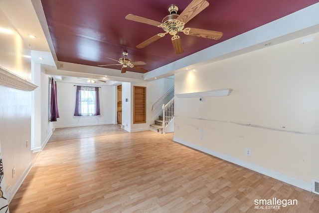 unfurnished living room featuring a tray ceiling, light hardwood / wood-style flooring, and ceiling fan