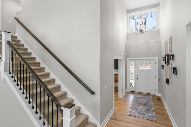 foyer featuring light wood finished floors, visible vents, baseboards, a towering ceiling, and a notable chandelier