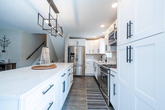 kitchen featuring white cabinets, dark wood finished floors, hanging light fixtures, stainless steel appliances, and a sink