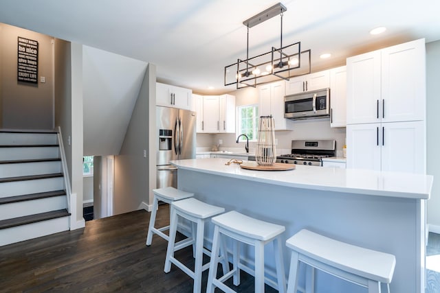 kitchen with white cabinets, appliances with stainless steel finishes, hanging light fixtures, light countertops, and a sink