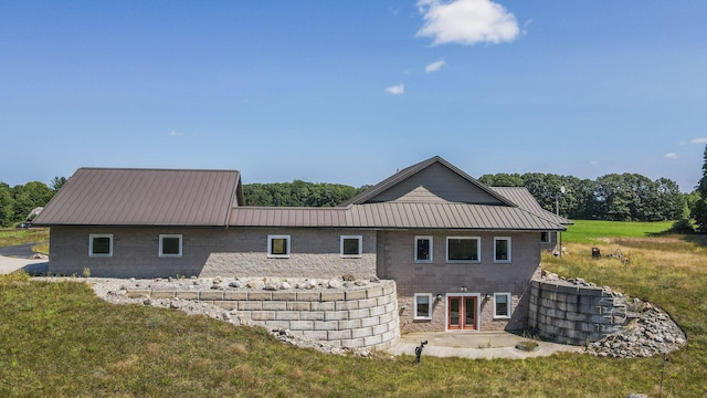 rear view of property with stone siding, a patio area, metal roof, and a lawn