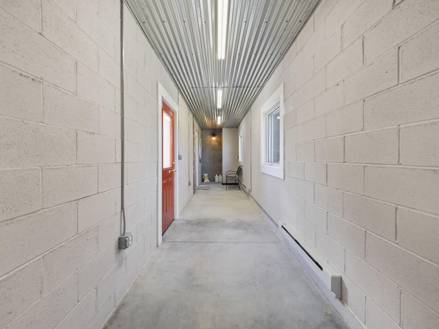 hallway with a baseboard heating unit, concrete block wall, and unfinished concrete floors