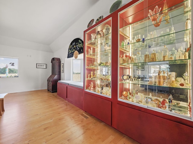 bar with a bar, vaulted ceiling, and wood finished floors