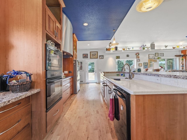 kitchen featuring light stone counters, a sink, dishwasher, light wood finished floors, and decorative light fixtures