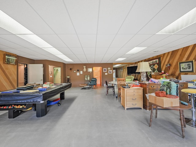 playroom featuring concrete flooring, a drop ceiling, and wooden walls