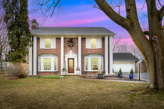 greek revival house with a garage, driveway, a chimney, a yard, and brick siding