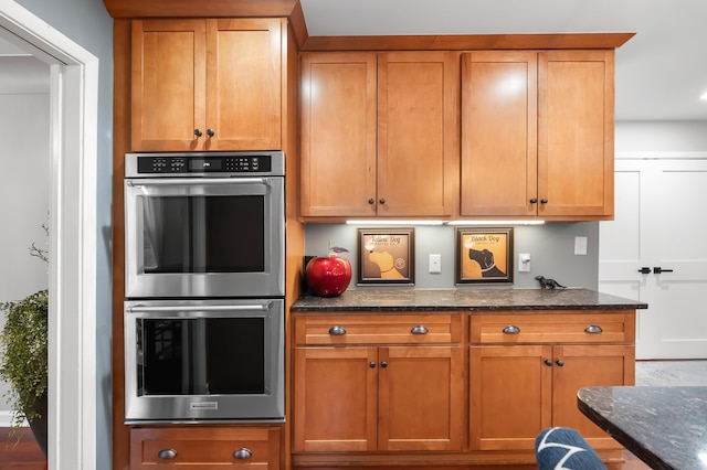 kitchen featuring dark stone counters, stainless steel double oven, and brown cabinetry