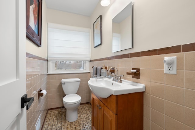 bathroom with a wainscoted wall, vanity, toilet, and tile walls