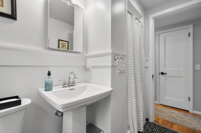 full bath with a shower with shower curtain, a wainscoted wall, a sink, and toilet