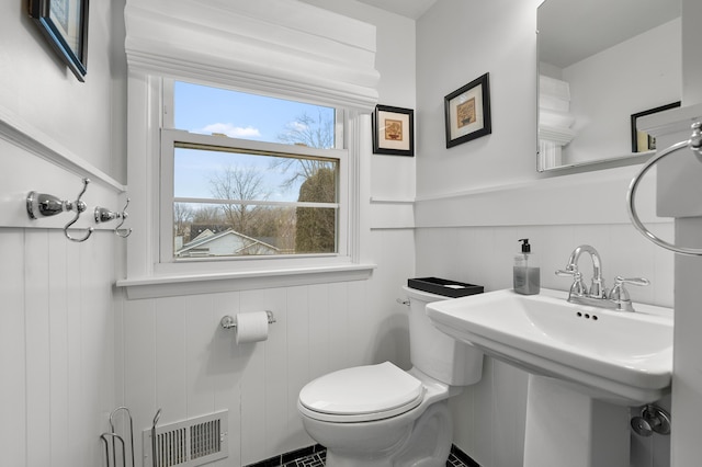 half bathroom with wainscoting, visible vents, and toilet