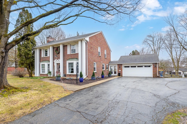 greek revival house featuring aphalt driveway, brick siding, a chimney, and an attached garage