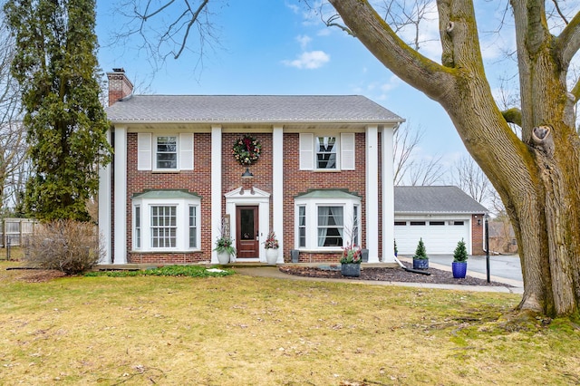 neoclassical / greek revival house with brick siding, a chimney, concrete driveway, an attached garage, and a front lawn