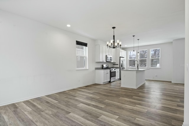 kitchen featuring white cabinetry, an island with sink, hanging light fixtures, hardwood / wood-style flooring, and stainless steel appliances