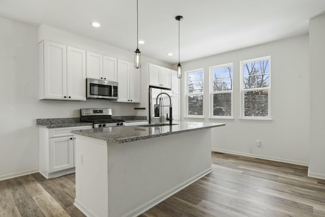 kitchen with appliances with stainless steel finishes, white cabinetry, sink, a kitchen island with sink, and light hardwood / wood-style floors