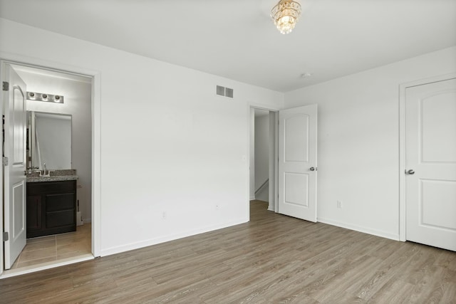 unfurnished bedroom with ensuite bathroom, sink, and light hardwood / wood-style floors