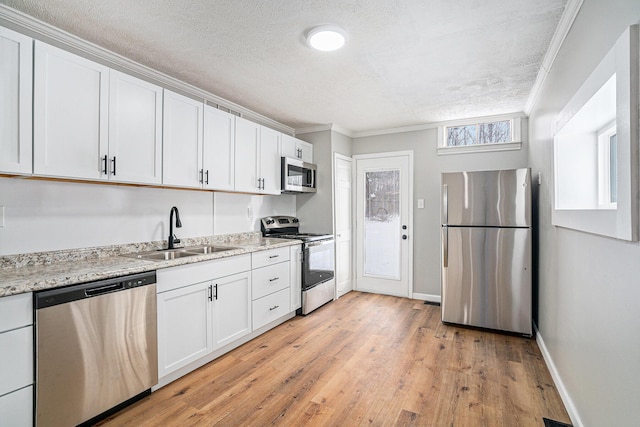 kitchen featuring stainless steel appliances, a sink, white cabinetry, light stone countertops, and crown molding