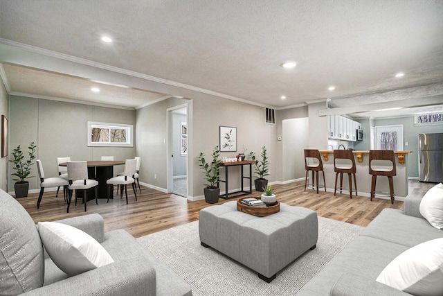 living area featuring baseboards, ornamental molding, bar, and light wood-style floors