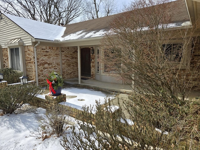 snow covered property entrance with brick siding