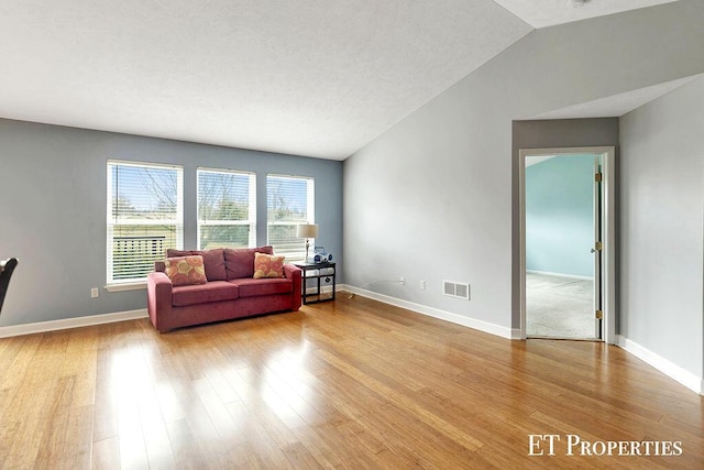 living area with visible vents, baseboards, light wood-style floors, and vaulted ceiling