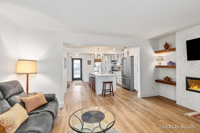 living area with light wood-style flooring, an inviting chandelier, a fireplace, and baseboards
