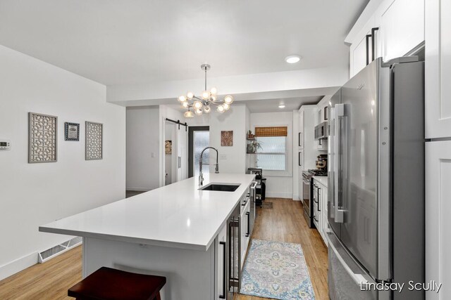 kitchen with white cabinets, a barn door, a sink, light wood finished floors, and stainless steel appliances