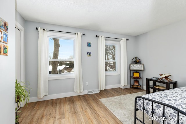 bedroom with visible vents, baseboards, a textured ceiling, and wood finished floors