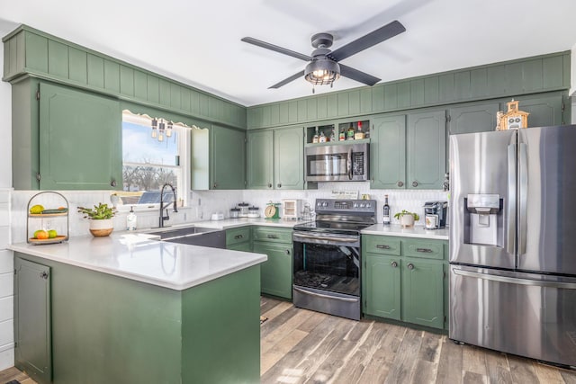 kitchen with appliances with stainless steel finishes, a sink, a peninsula, and green cabinets