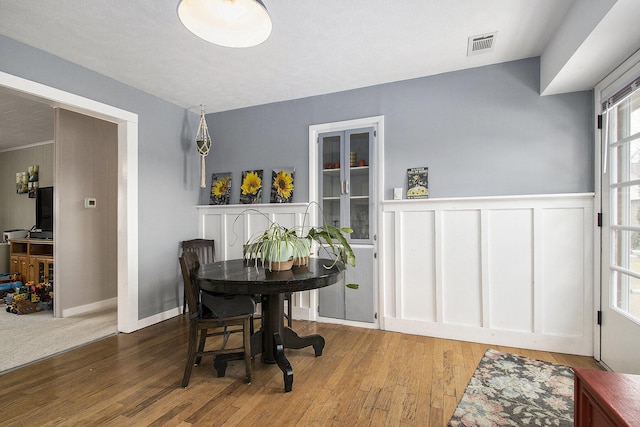 dining space featuring a wainscoted wall, visible vents, a decorative wall, and wood finished floors