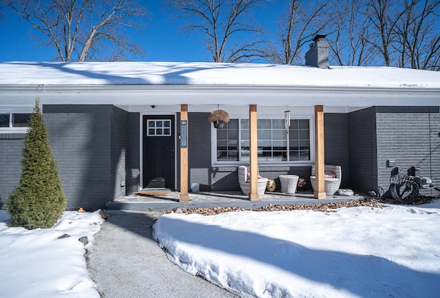 snow covered property entrance featuring a chimney and brick siding